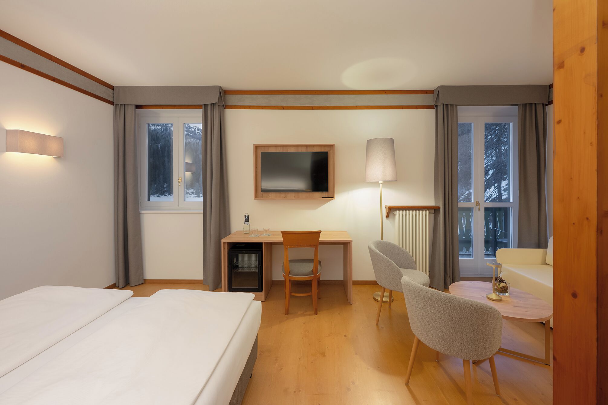 A hotel room with a bed, a desk, a chair, a lamp, and a view of the outdoors.