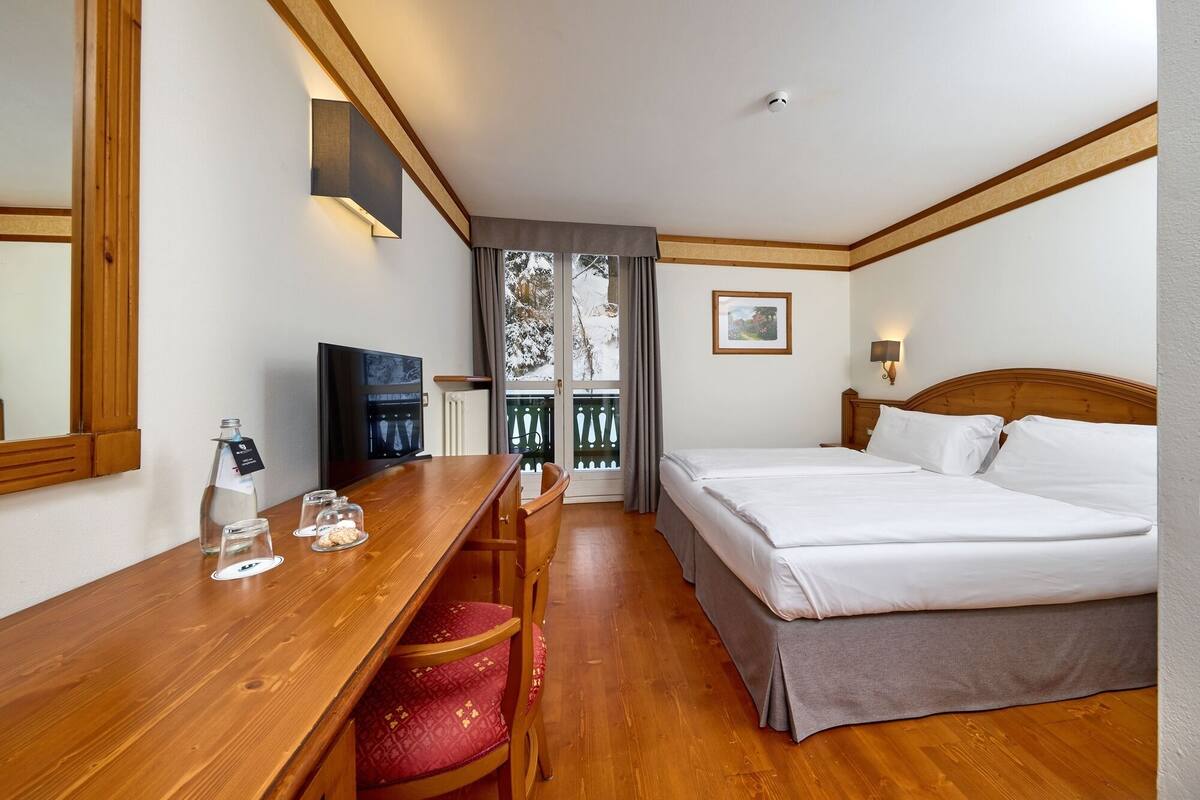 Une chambre d’hôtel avec un bureau en bois, un lit, une télévision et une fenêtre donnant sur des arbres.