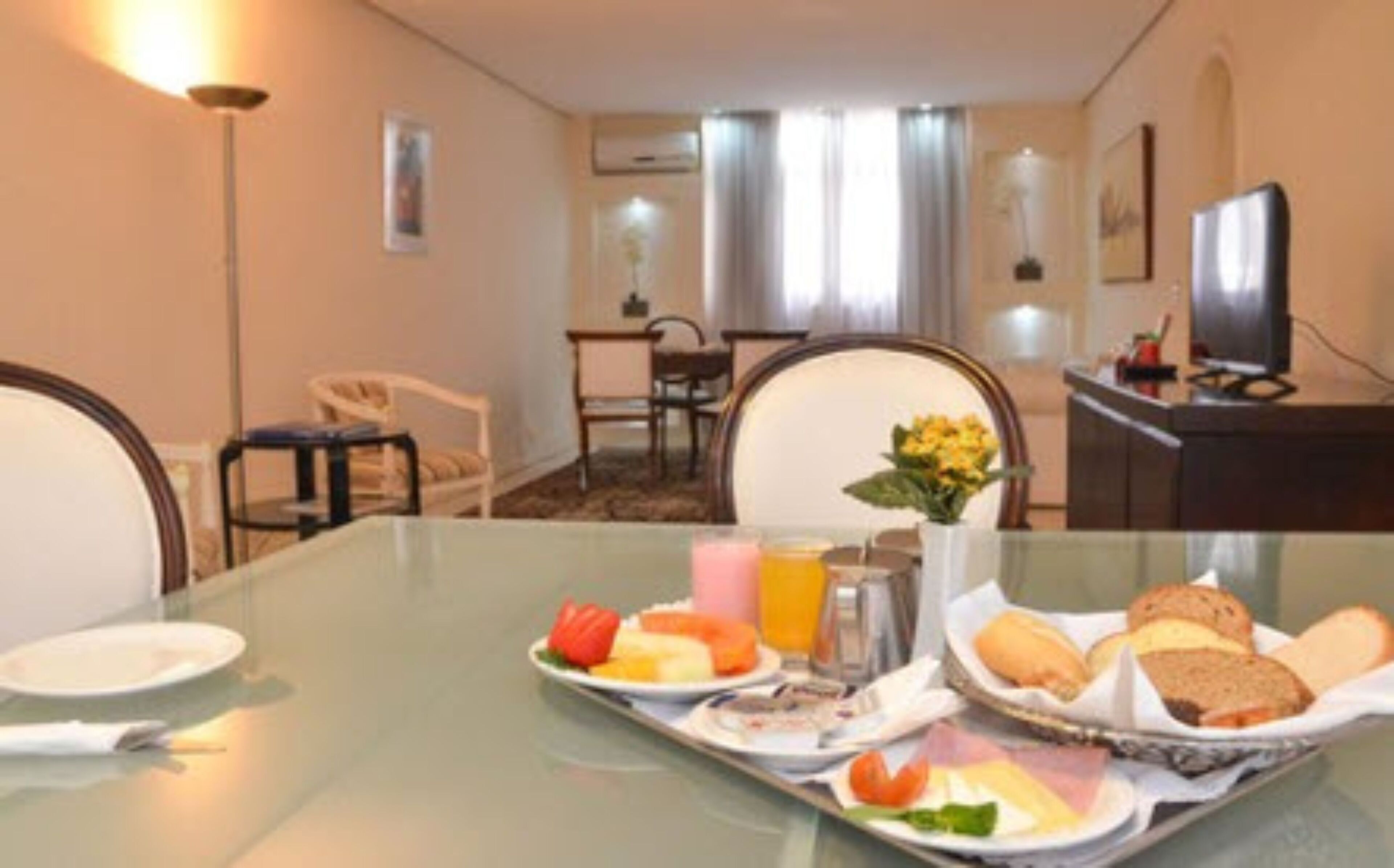 A hotel room with a dining table set with breakfast items, a television, and a desk with a computer.