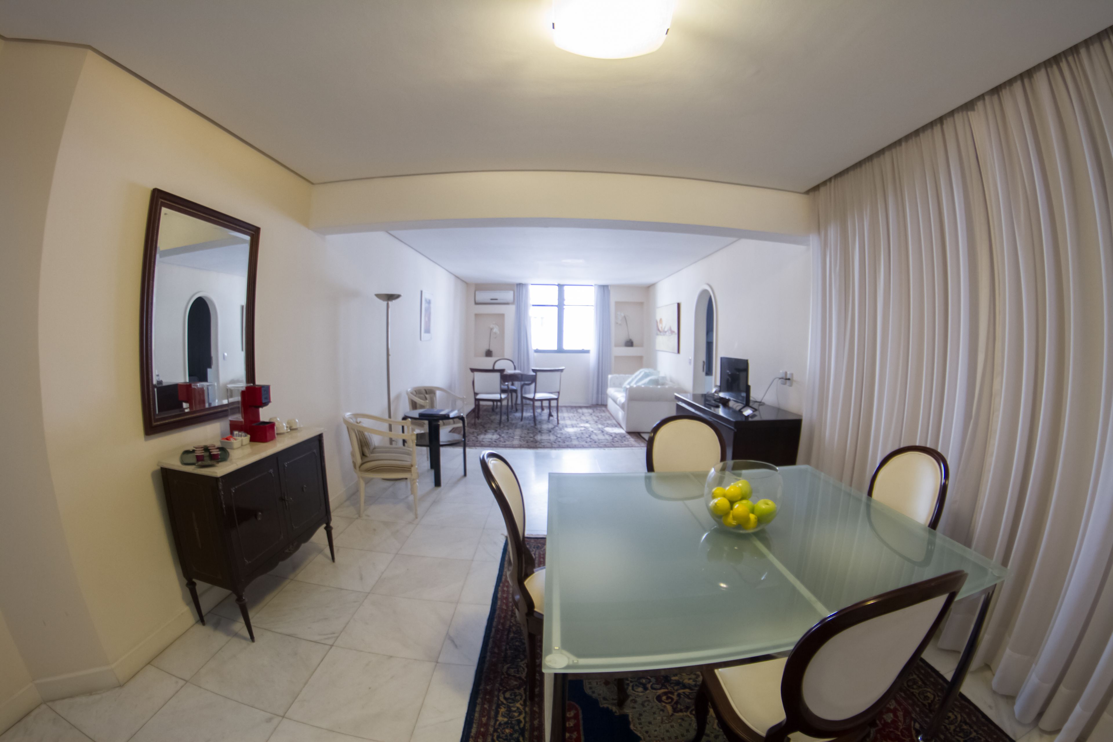 Comedor con mesa de vidrio, sillas, espejo, cómoda y vista a otra habitación.