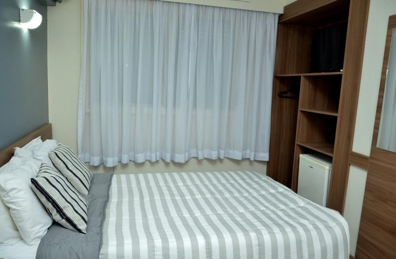 Un dormitori amb un llit, almoines, un armari i una finestra amb cortines.