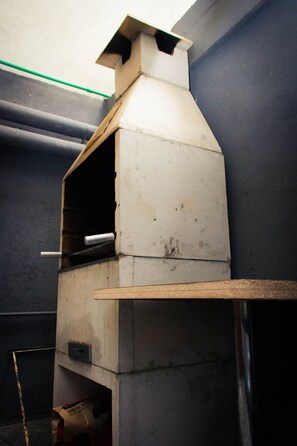 A metal outdoor pizza oven with a chimney, a wooden shelf, and a small storage compartment. - Hotel Embaixador (Porto Alegre)
