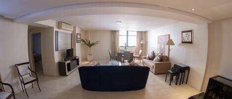A spacious living area with a dark sofa, a dining table, and a TV.