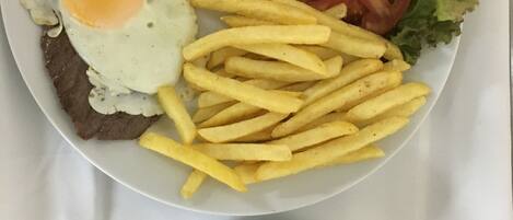 A plate with a fried egg, beef, rice, French fries, tomato slices, lettuce, and a small bowl of sauce.