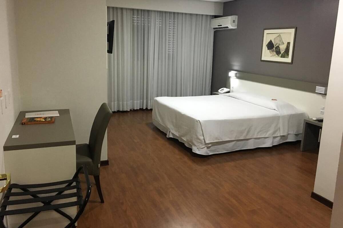 A hotel room with a bed, desk, chair, and curtains.