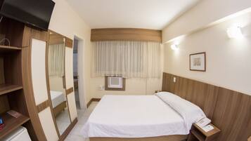 Quarto de hotel com cama, televisão, guarda-roupa, espelho, mesa de cabeceira com telefone e janela com cortinas.