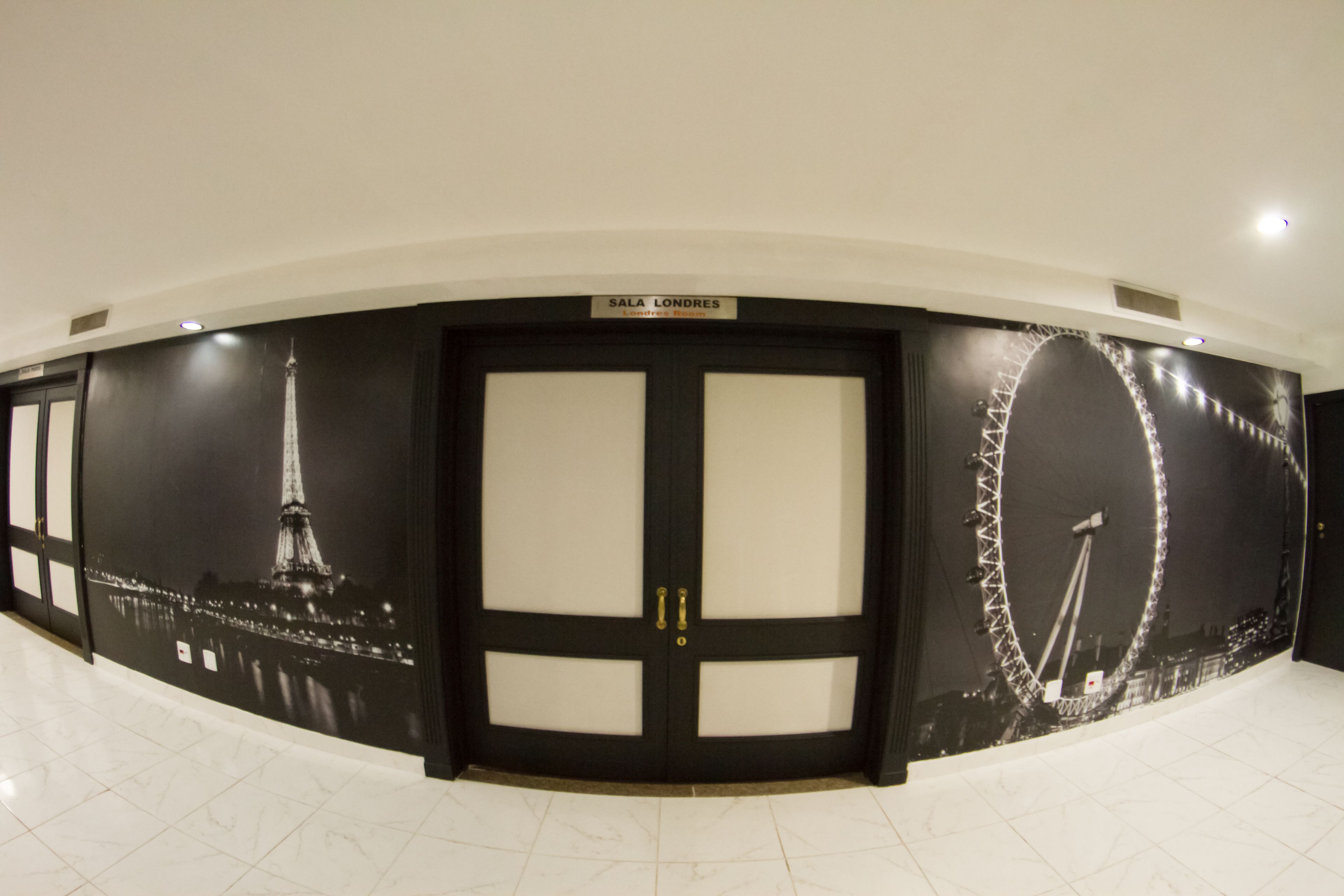 Un pasillo con un mural en blanco y negro de la Torre Eiffel y una noria, un letrero que dice 'Sala Londres', y un piso de baldosas.