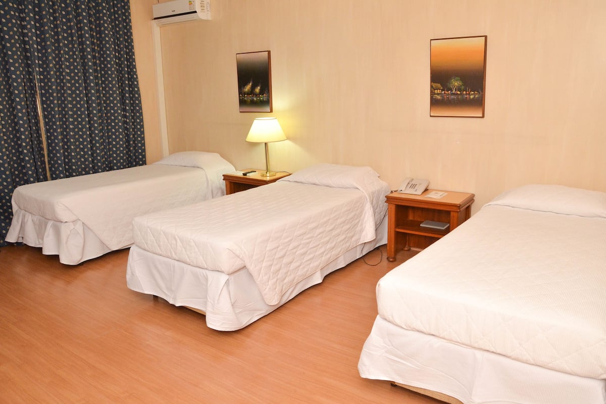 A hotel room with two single beds, a bedside table with a lamp, a phone, and a wall-mounted air conditioner.