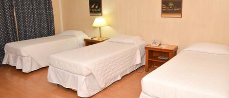Quarto de hotel com duas camas de solteiro, uma mesa de cabeceira com luminária, telefone e ar condicionado fixado na parede.