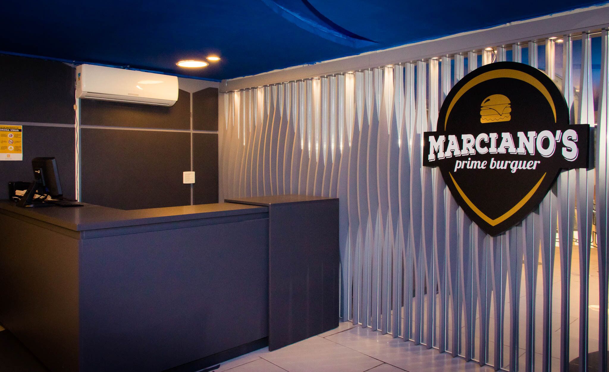 Zona de recepción con mostrador, equipo de aire acondicionado y un letrero de Marciano's Prime Burguer.