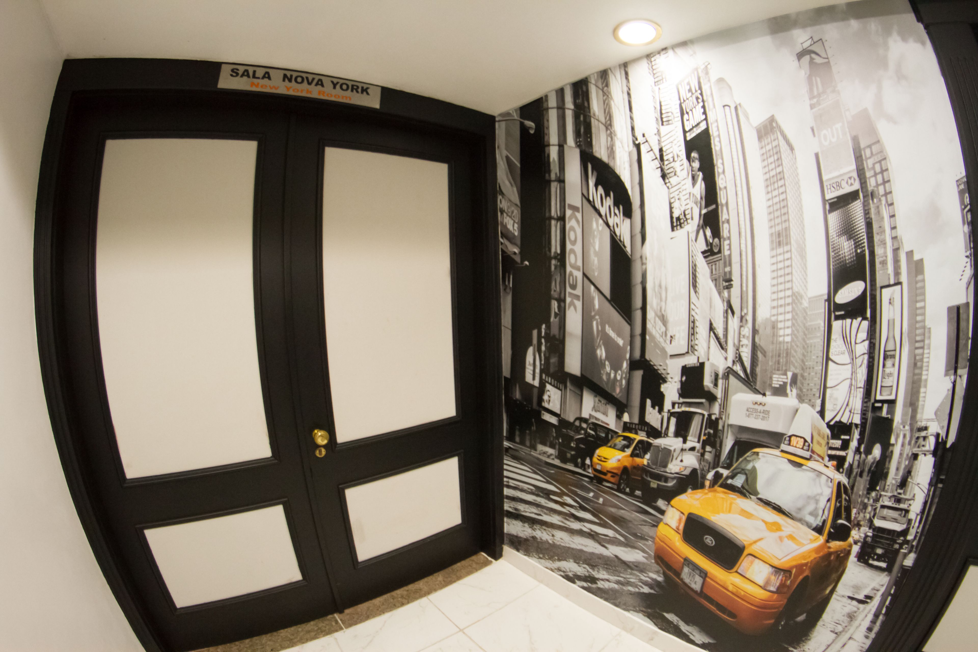 A hallway with a black door labeled "SALA NOVA YORK" and a mural of a city street with taxis.