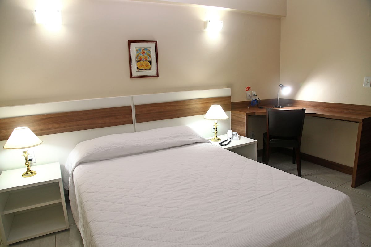 A hotel room with a bed, two bedside tables with lamps, a desk, and a chair.