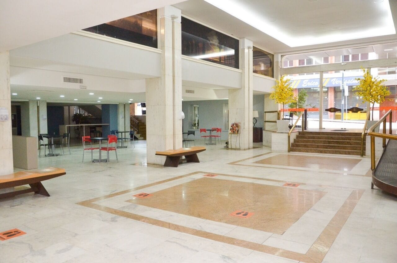 Een ruime lobby met hoge plafonds, een centrale trap en een zithoek met tafels en stoelen.