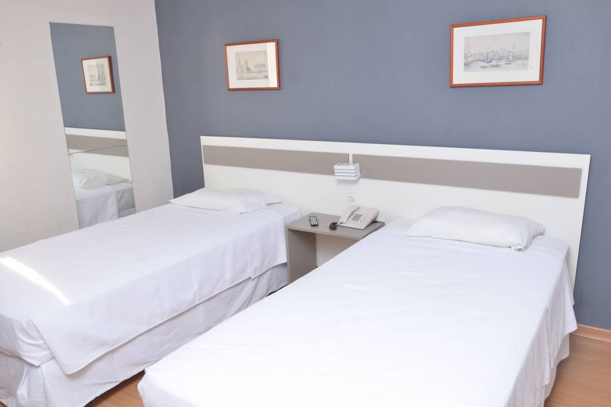 A hotel room with two single beds, a bedside table with a phone, and framed pictures on the wall.
