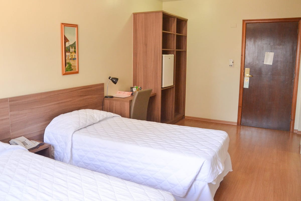 A hotel room with two beds, a desk with a chair, a wardrobe, and a door.