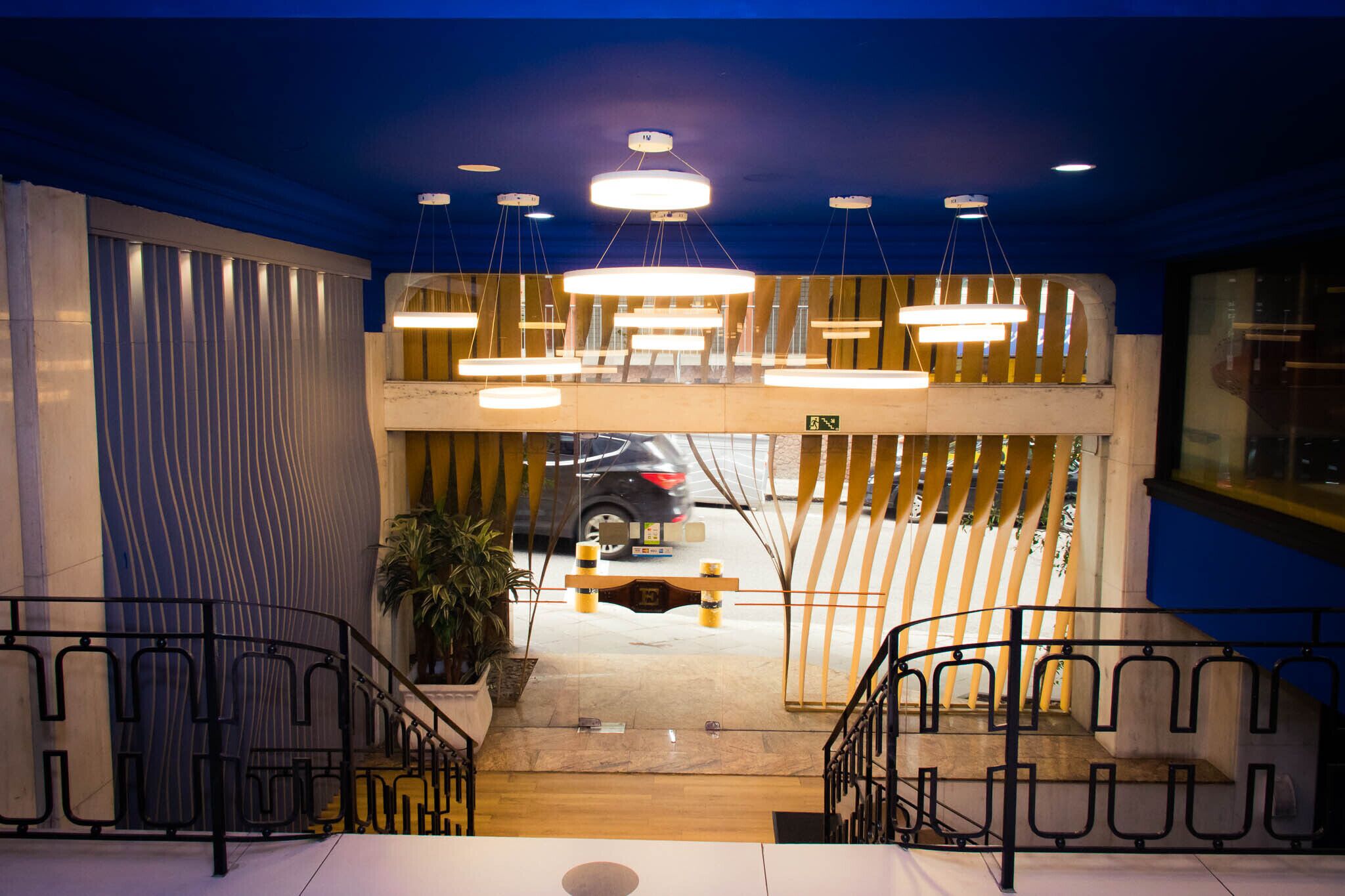 A hotel entrance with a double staircase, modern lighting, and a car parked outside.