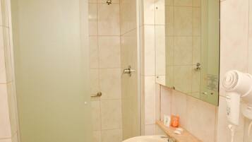 A bathroom with a shower, sink, and a hairdryer on the counter.