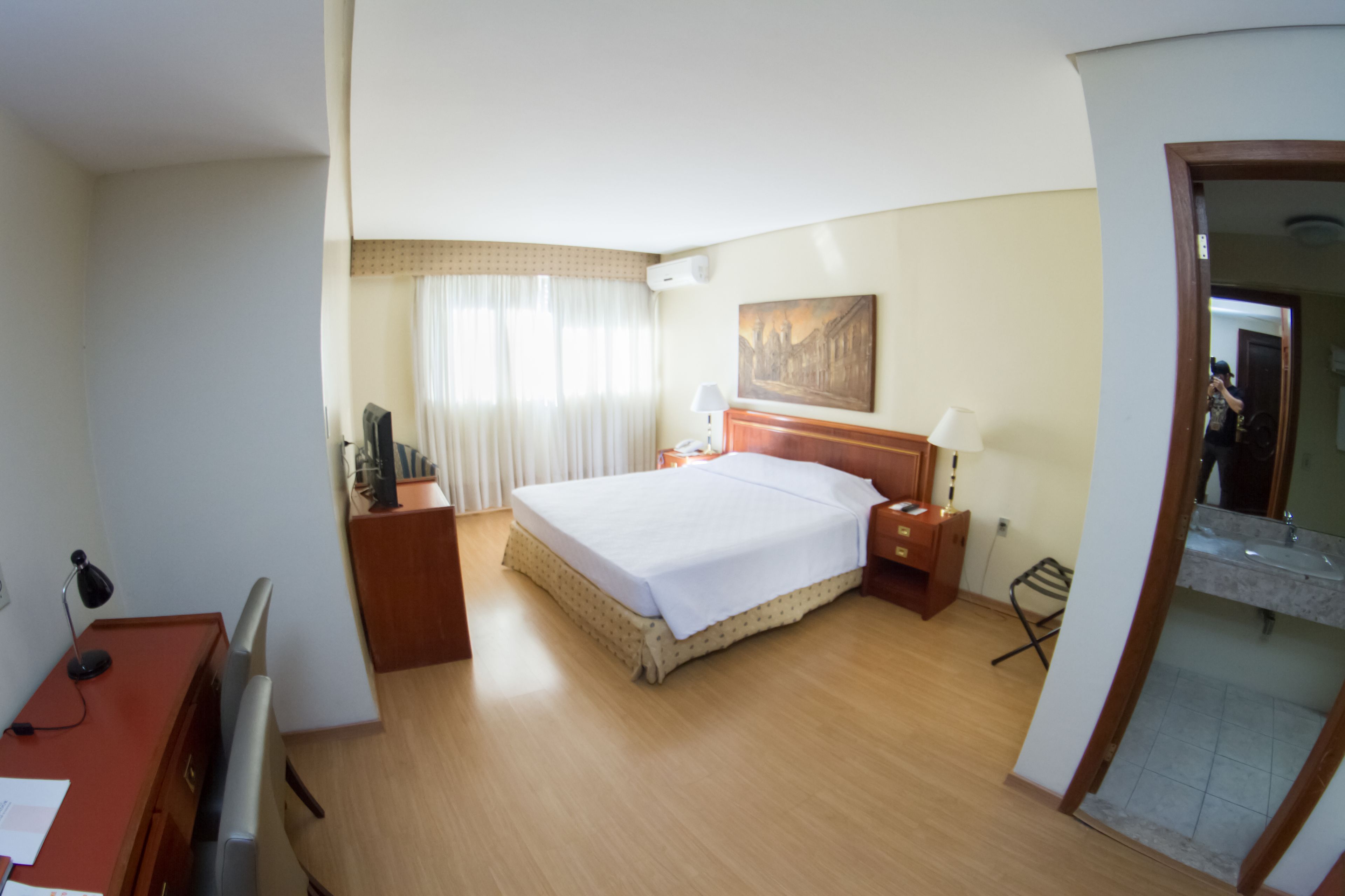Una habitación de hotel con cama, escritorio, silla, lámpara y espejo.