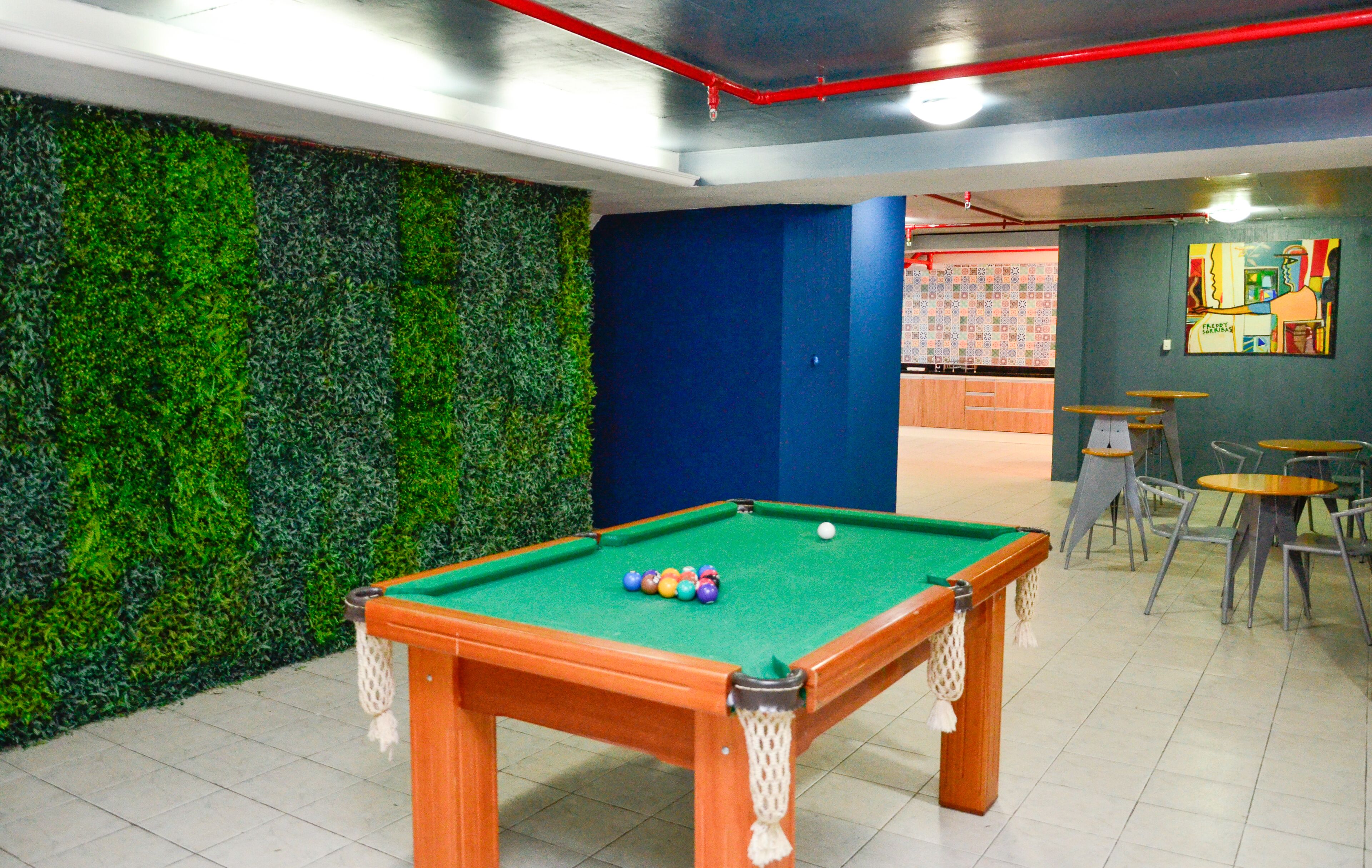 Uma mesa de bilhar com bolas, uma parede verde e uma porta azul em um espaço com piso ladrilhado.