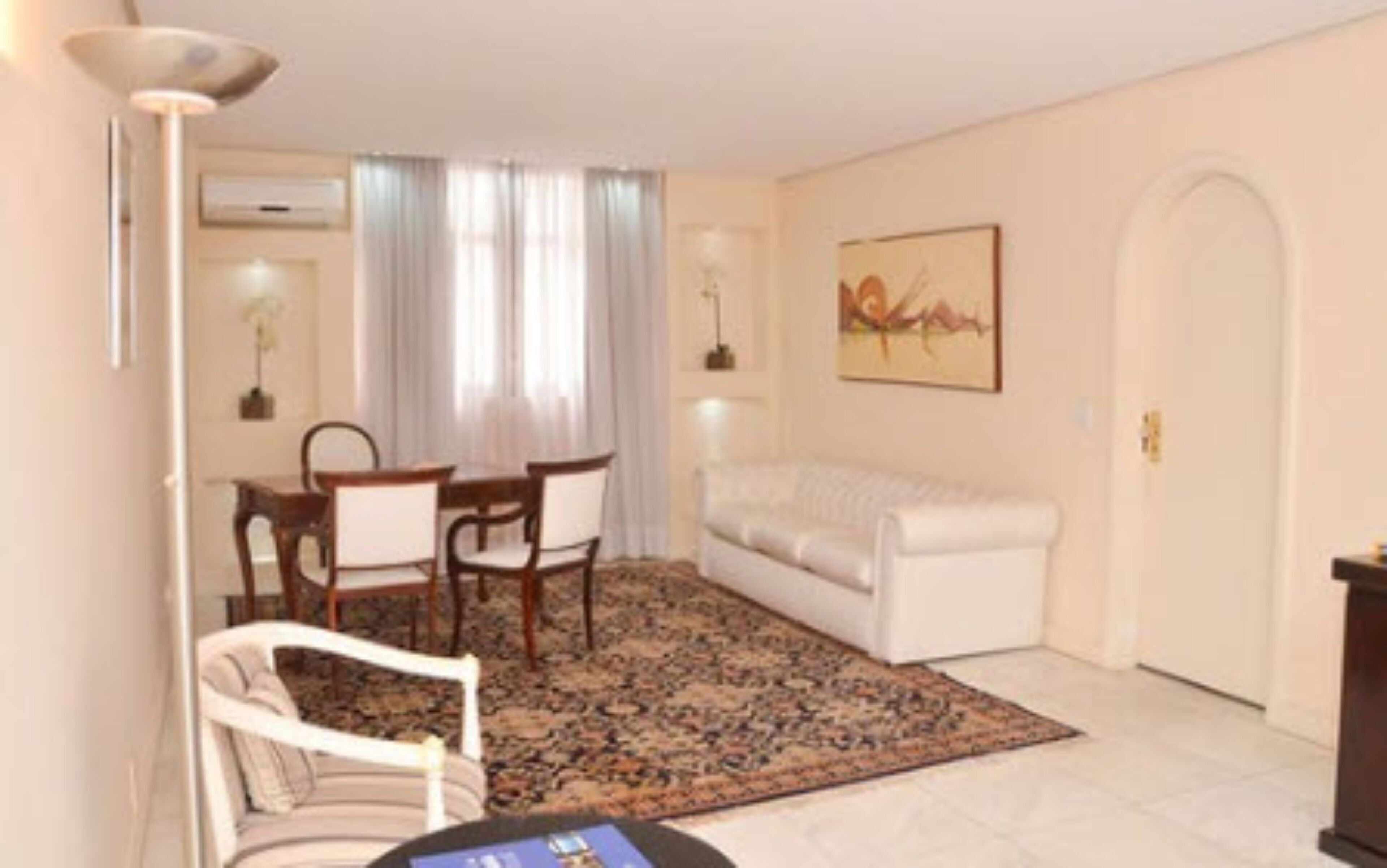 A living room with a white sofa, a dining table with chairs, a patterned rug, and a painting on the wall.