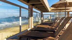 A sun deck with lounge chairs and umbrellas overlooking a beach and cityscape. - Parque Balneário Hotel Santos by Castelo Itaipava (Santos)