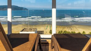 A beach view from a room with two wooden chairs, a small pool, and a sandy beach area with umbrellas. - Parque Balneário Hotel Santos by Castelo Itaipava (Santos)