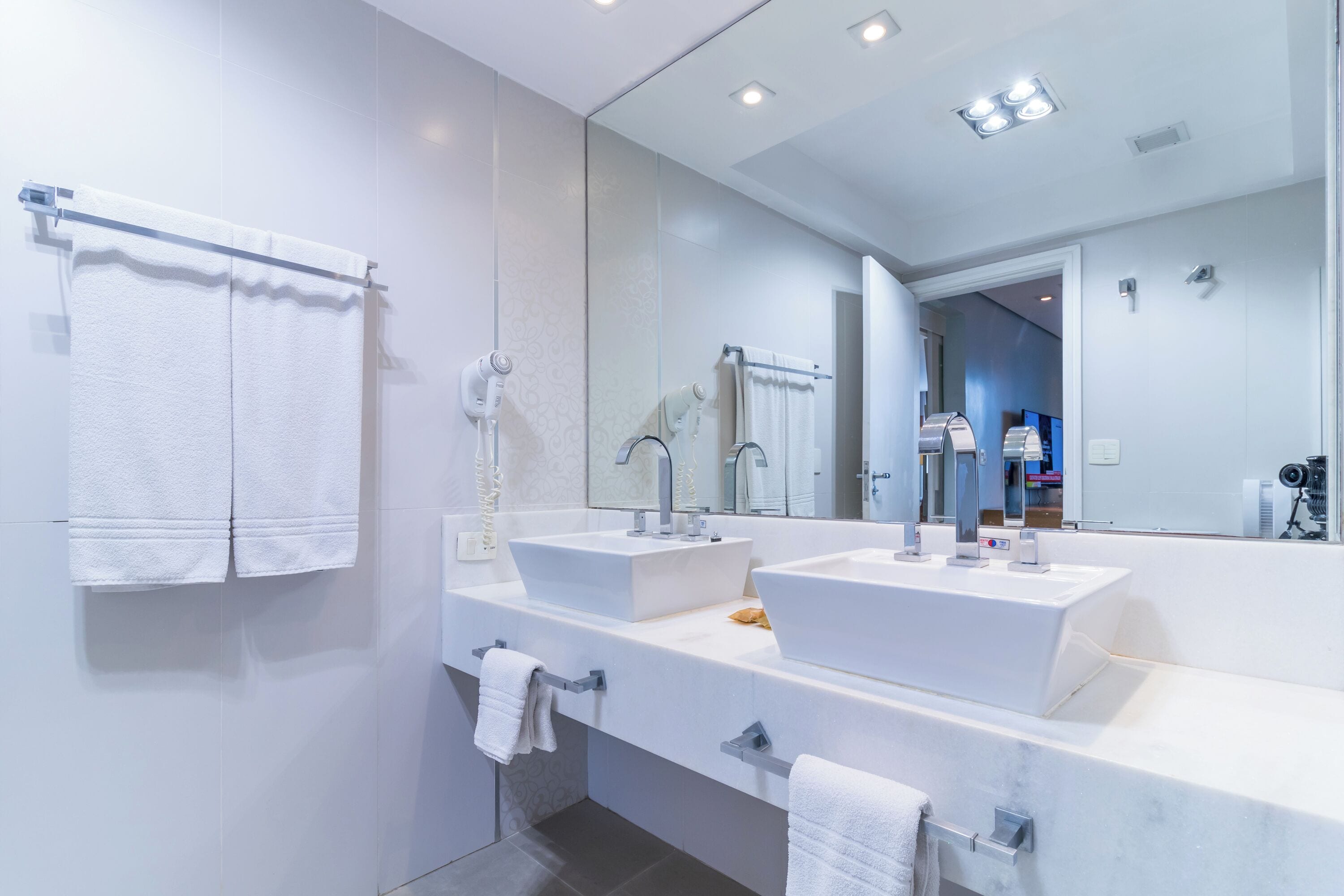 A modern bathroom with two sinks, a large mirror, and towels on hooks.