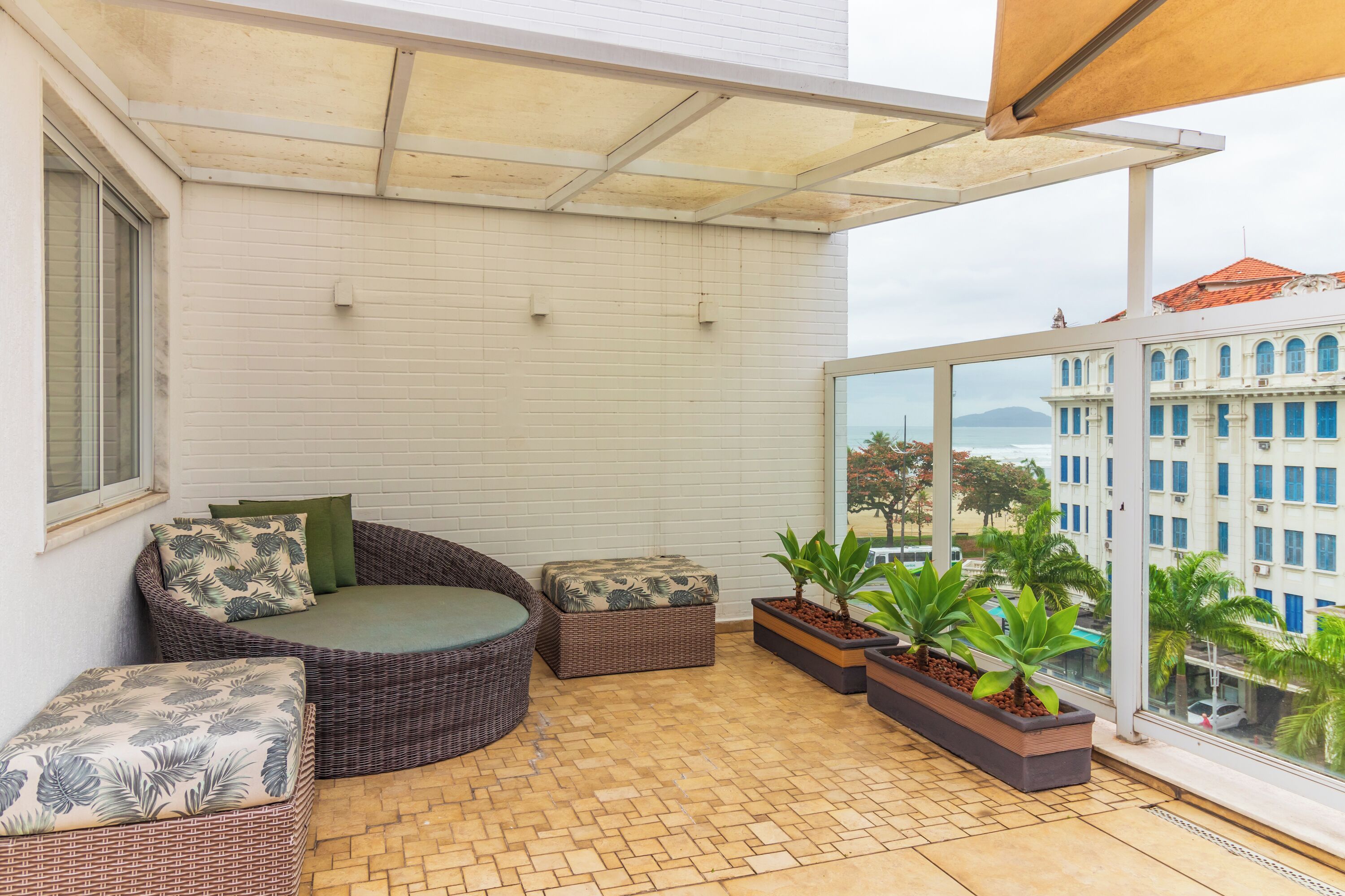 A balcony with wicker furniture, potted plants, and a view of a building across the street.