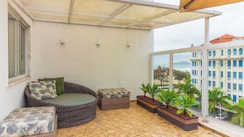 A balcony with wicker furniture, potted plants, and a view of a building across the street.