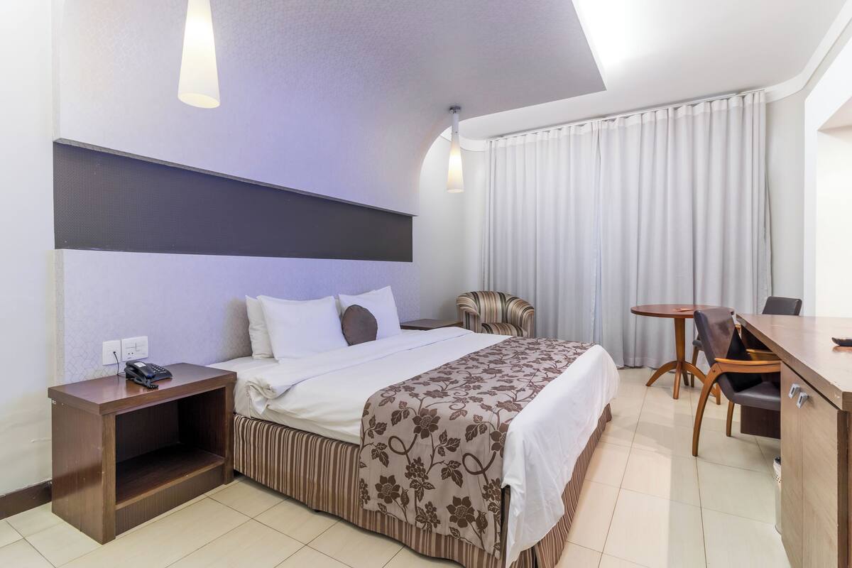 A hotel room with a bed, bedside table, lamp, and a small table with chairs.