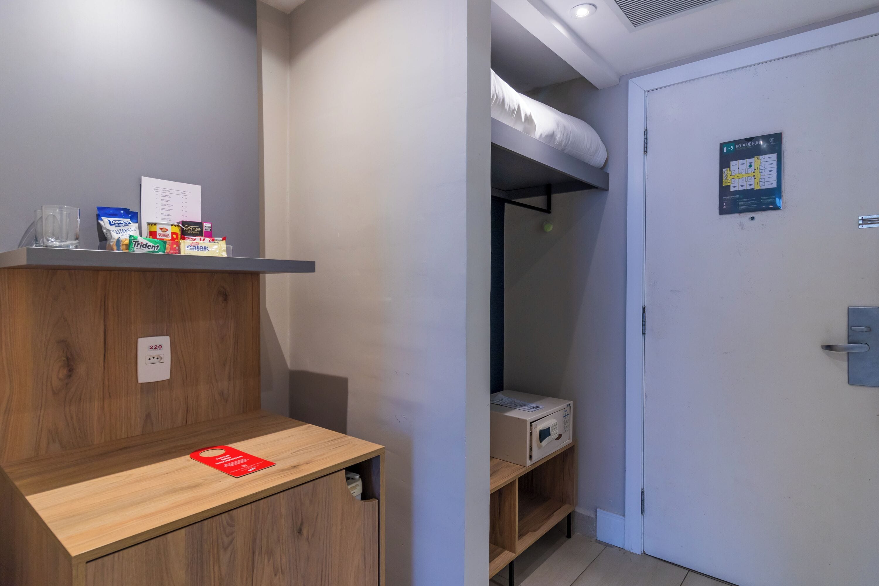 Une chambre d’hôtel avec un bureau en bois, une étagère avec des collations, un lit superposé et une porte ornée d’une carte.