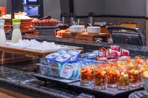 Un bufé con diversas opciones de comida, como frutas, yogur y pan.
