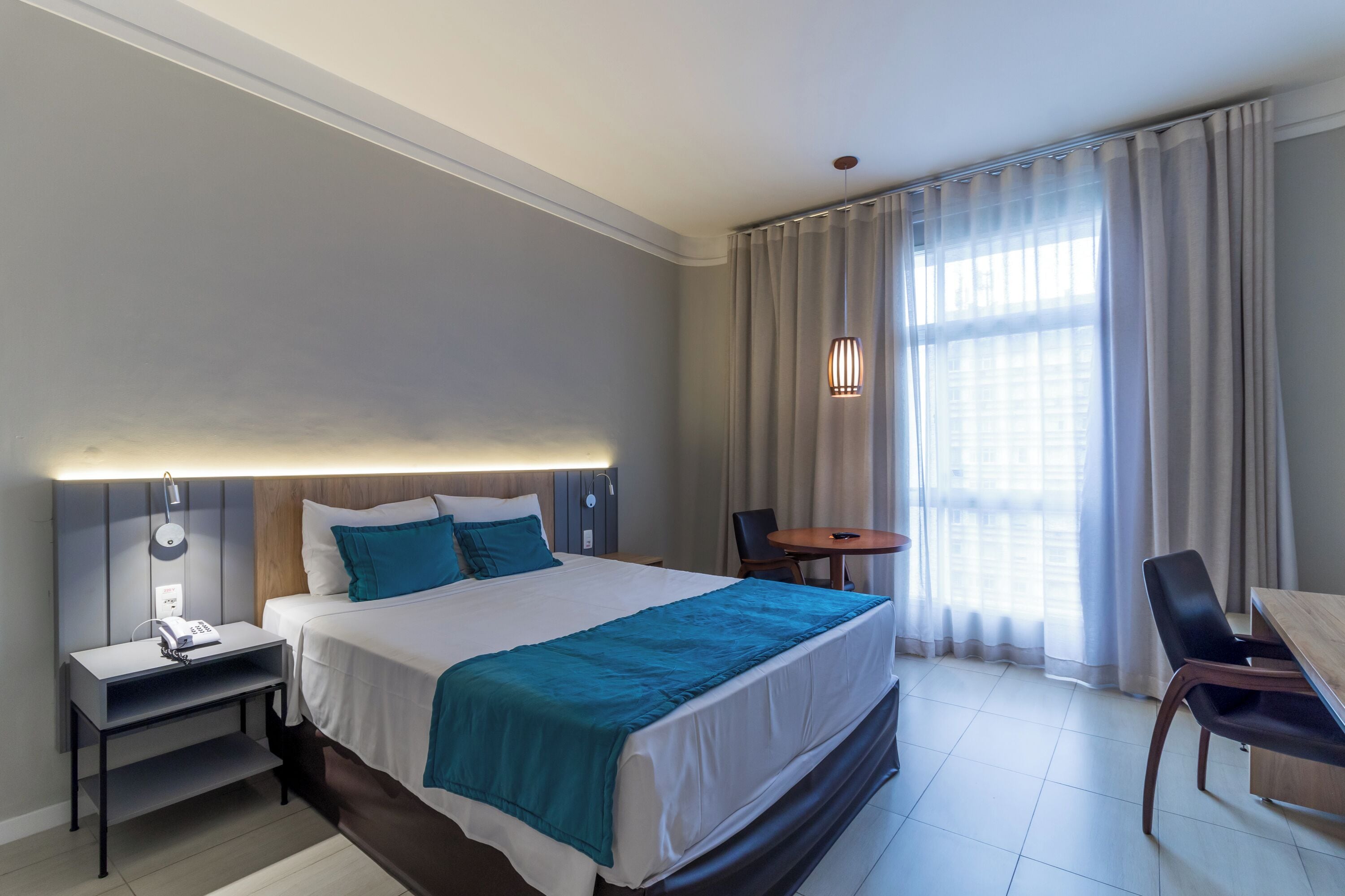 A hotel room with a large bed, bedside table, lamp, and a small table with chairs.