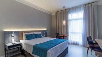 A hotel room with a large bed, bedside table, lamp, and a small table with chairs.