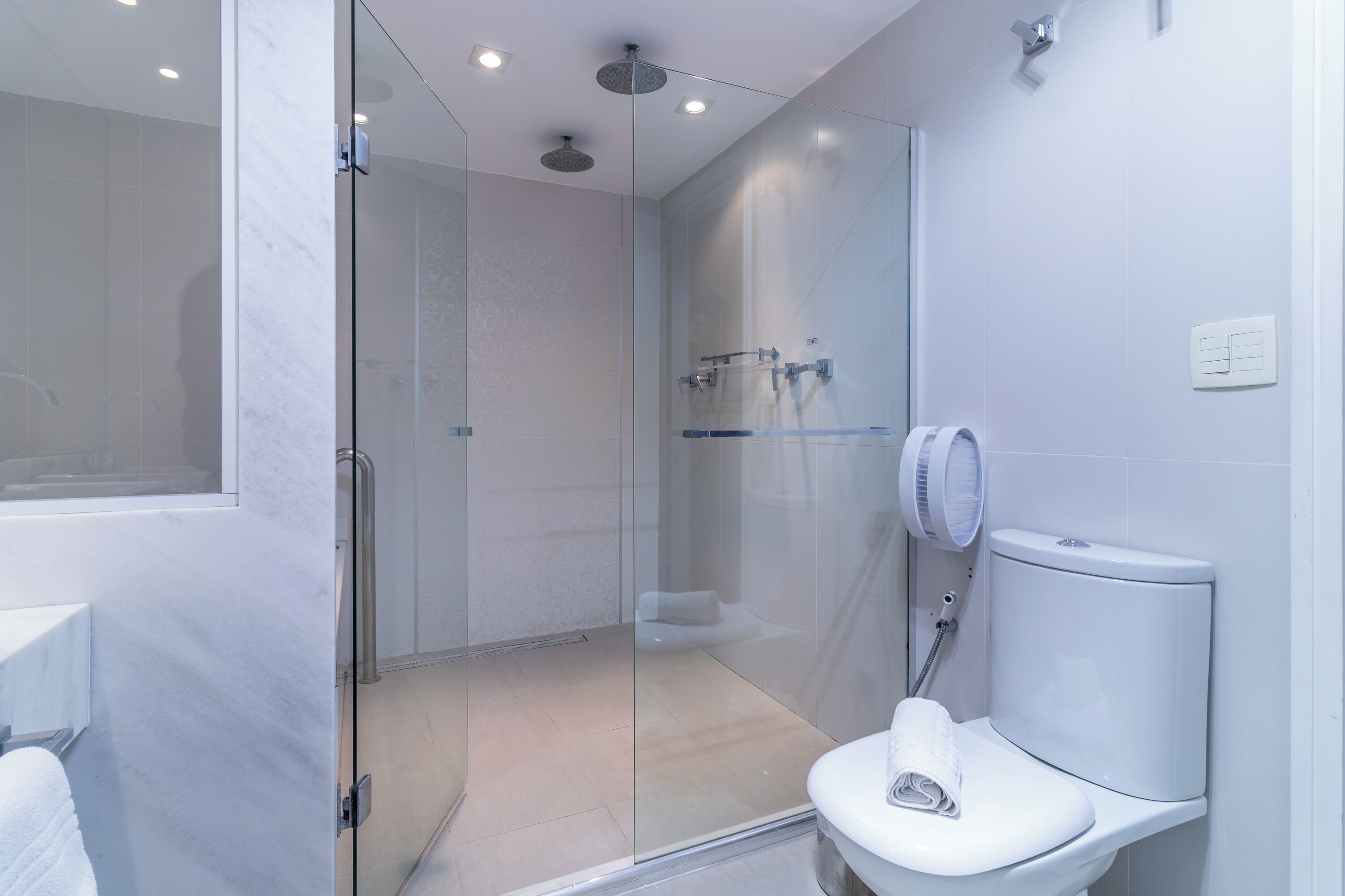 Un baño moderno con ducha de vidrio, inodoro blanco y toallero visible.