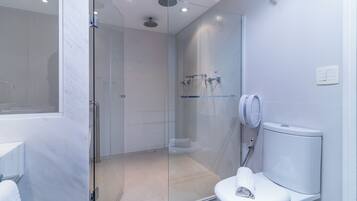 Un baño moderno con ducha de vidrio, inodoro blanco y toallero visible.
