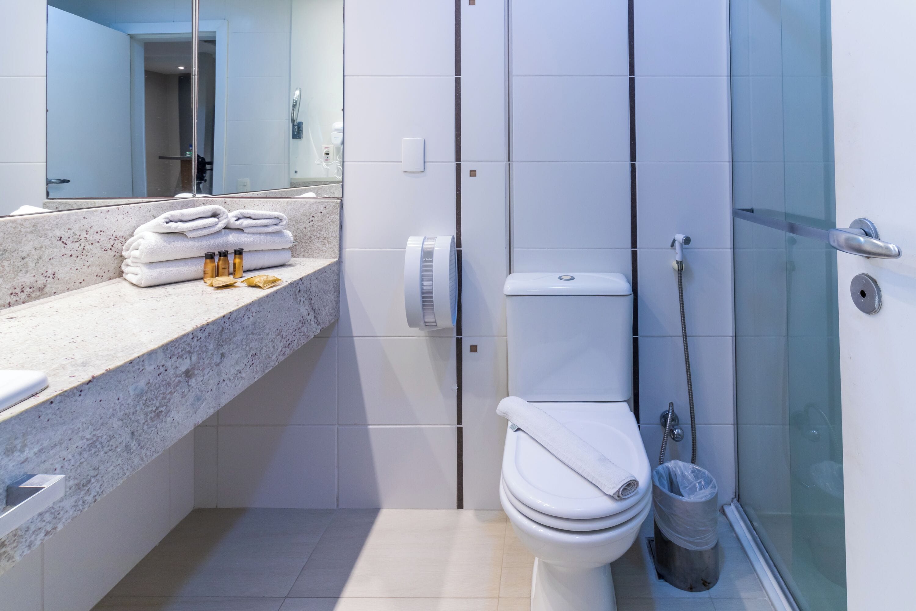Een moderne badkamer met een wit toilet, een douchecabine van glas en een marmeren aanrecht met handdoeken en toiletartikelen.