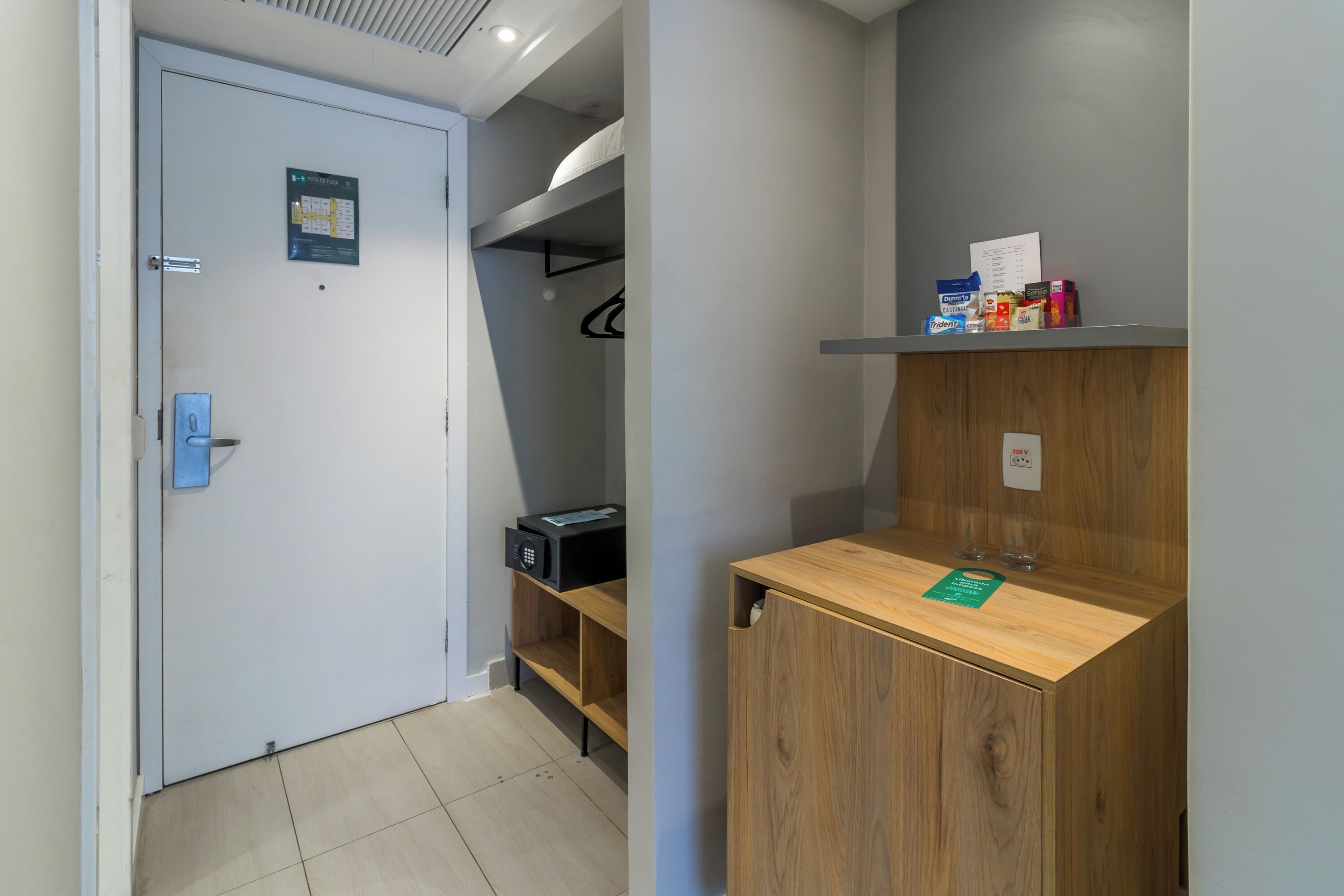 Ein Hotelzimmer mit einem Holzschrank, einem Ablagefach für Toilettenartikel, einer Tür mit Kartenlesegerät und einem kleinen Schreibtisch mit einem grünen Schild.