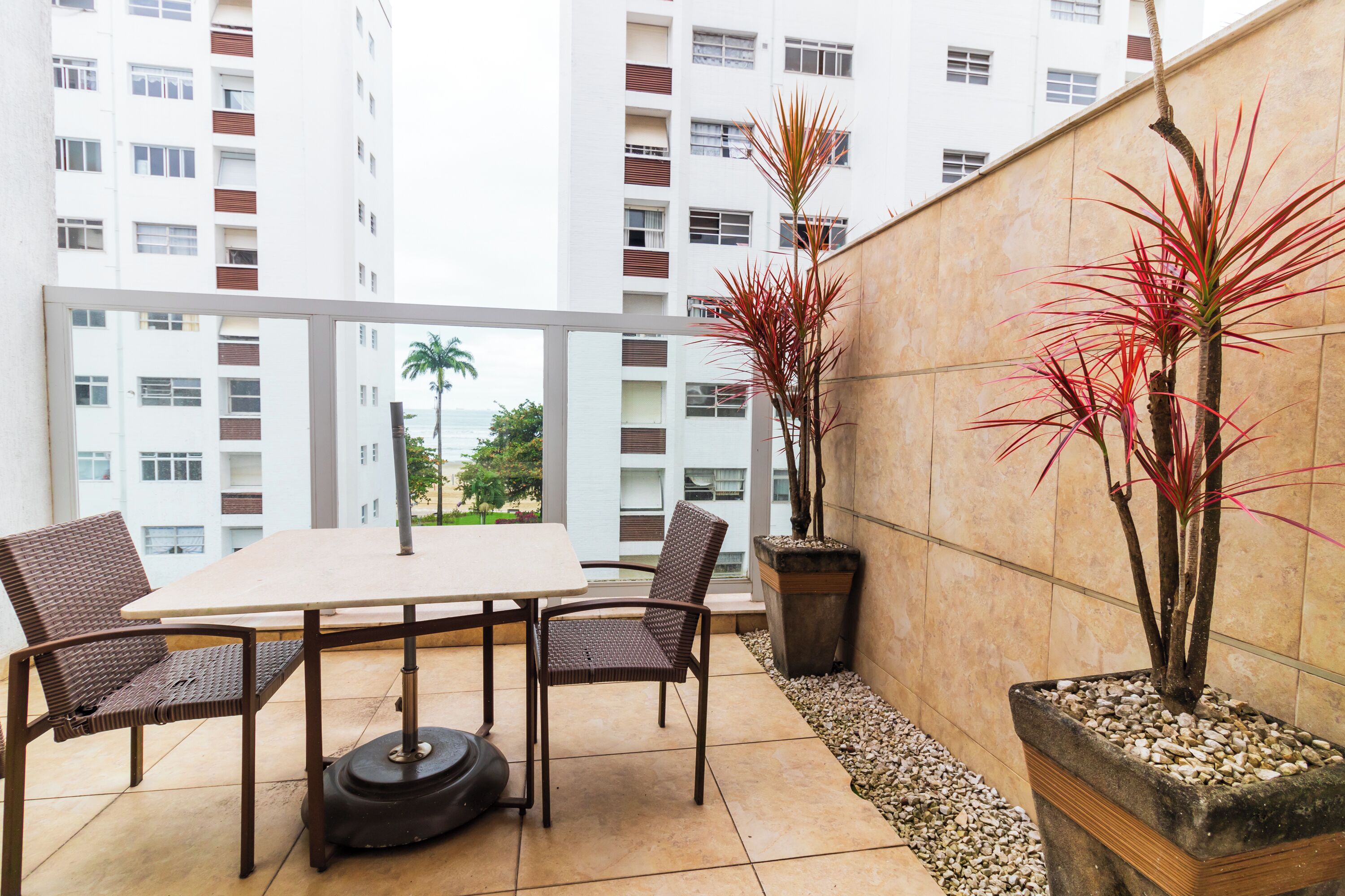 A balcony with a table and chairs, a potted plant, and a view of a tall building.