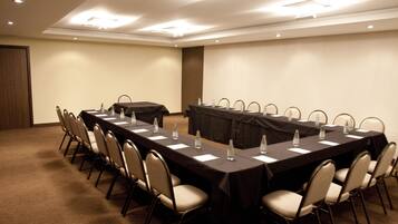 Un salón de conferencias con una mesa larga, sillas y botellas de agua.