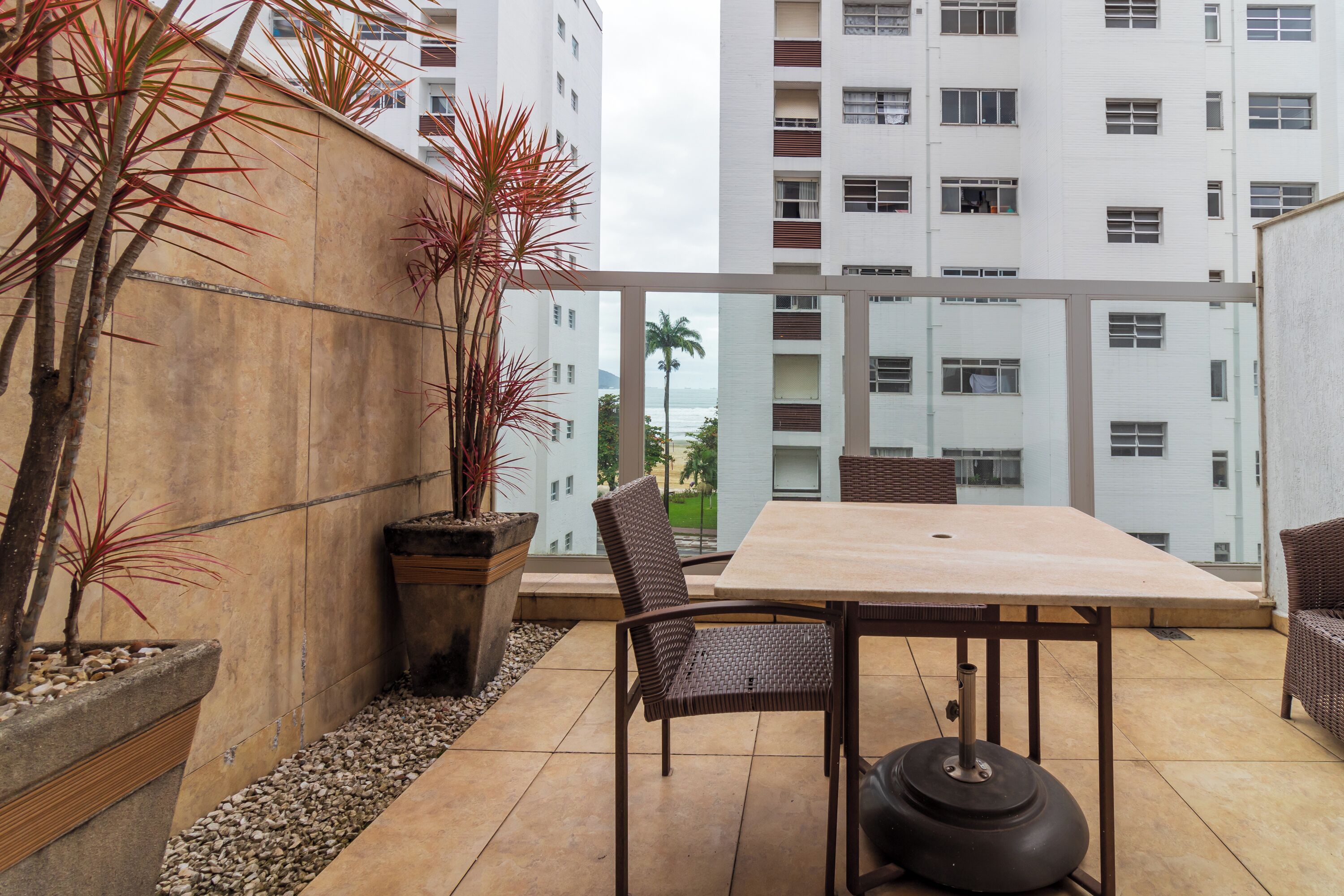 Een balkon met een tafel en stoelen, plantenbakken en uitzicht op een hoog gebouw.
