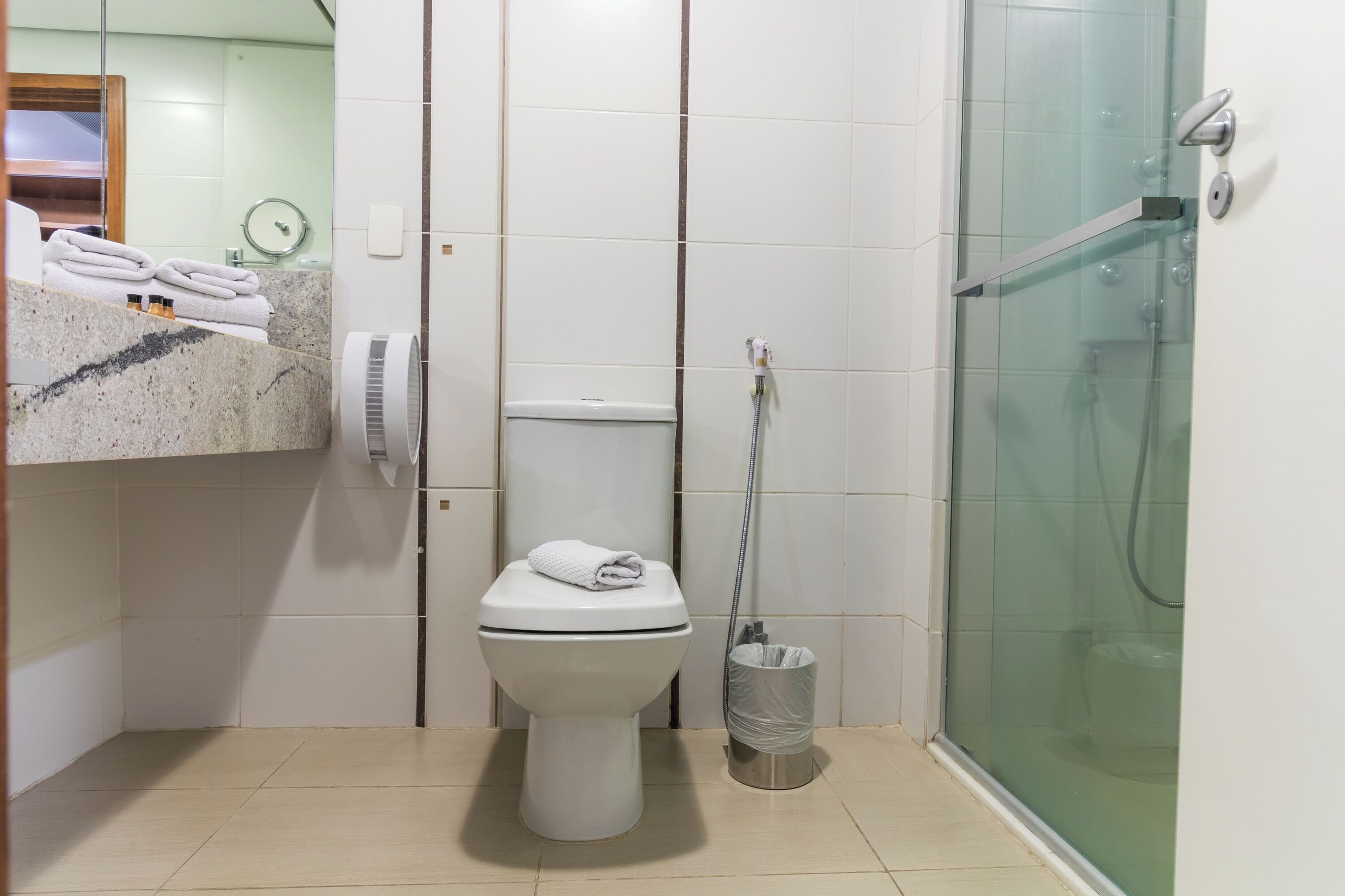 Casa de banho com sanita, cabine de duche em vidro, um porta-toalhas com toalhas e um contentor de lixo.