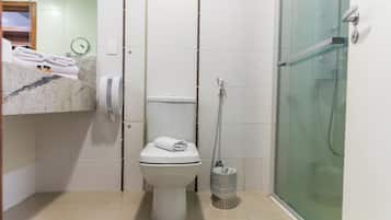 Casa de banho com sanita, cabine de duche em vidro, um porta-toalhas com toalhas e um contentor de lixo.