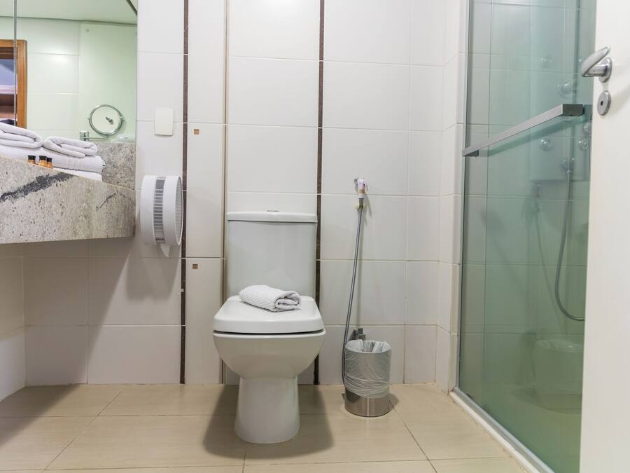Casa de banho com sanita, cabine de duche em vidro, um porta-toalhas com toalhas e um contentor de lixo.