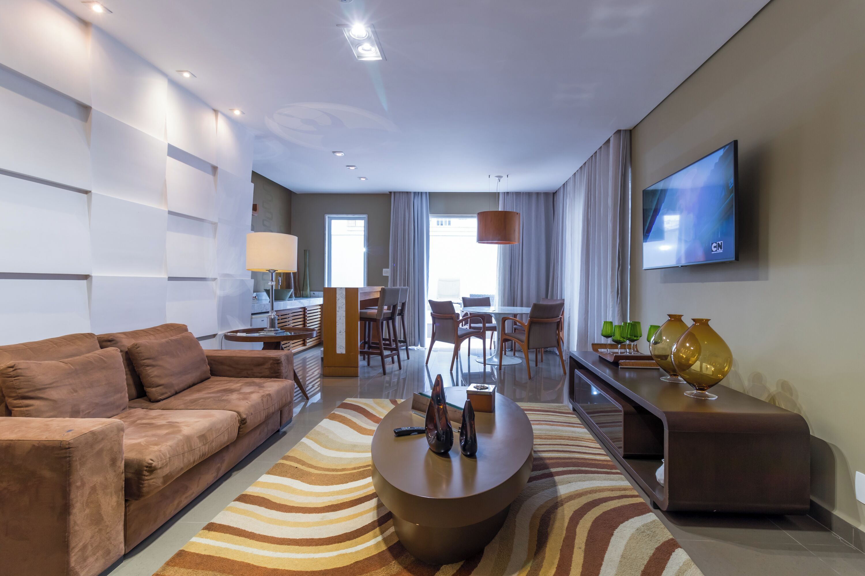 Un salon moderne avec un canapé, une table basse et un téléviseur. On aperçoit à l’arrière-plan un coin repas avec des chaises et une table.