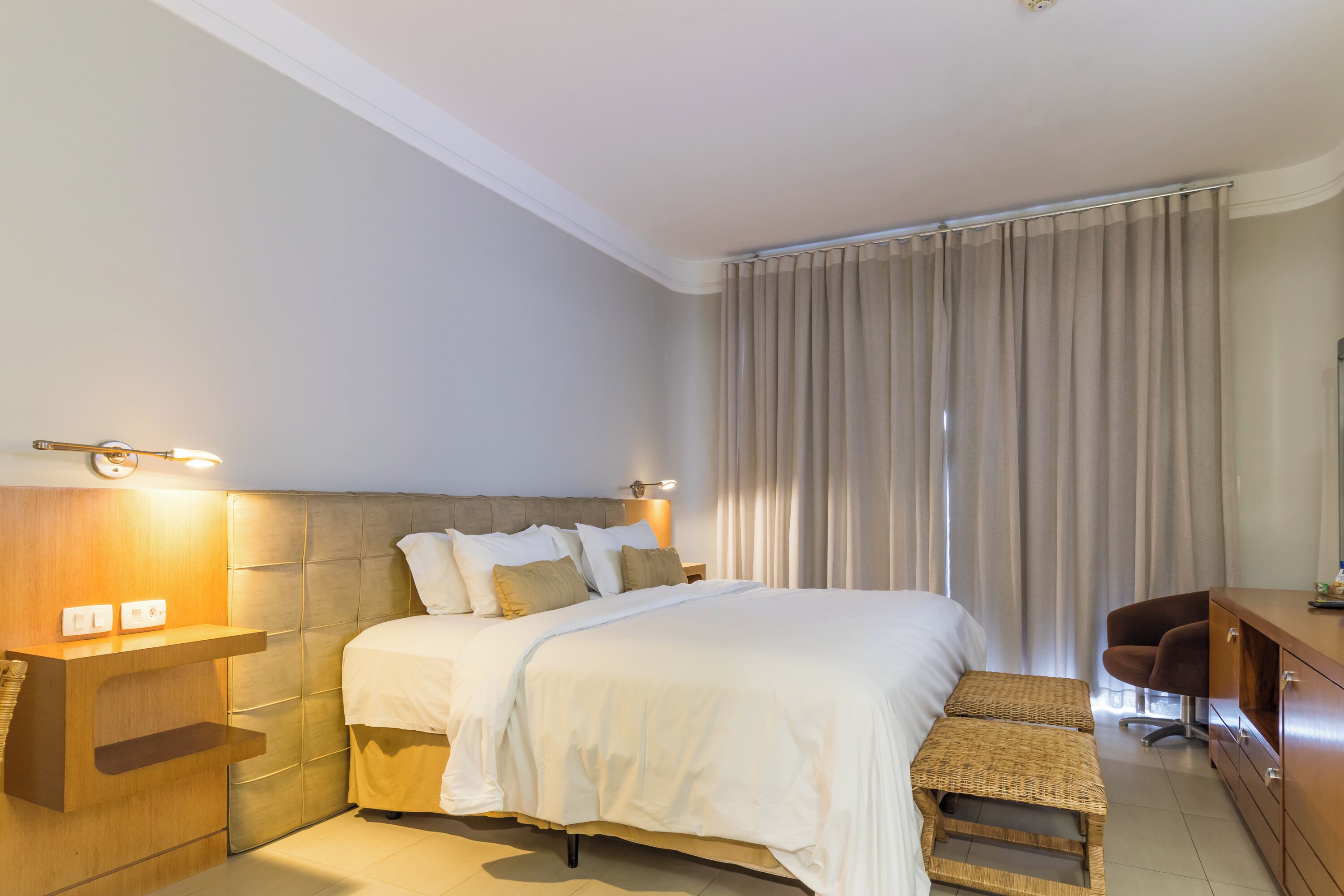 A hotel room with a bed, bedside table, lamp, and a desk with a chair.