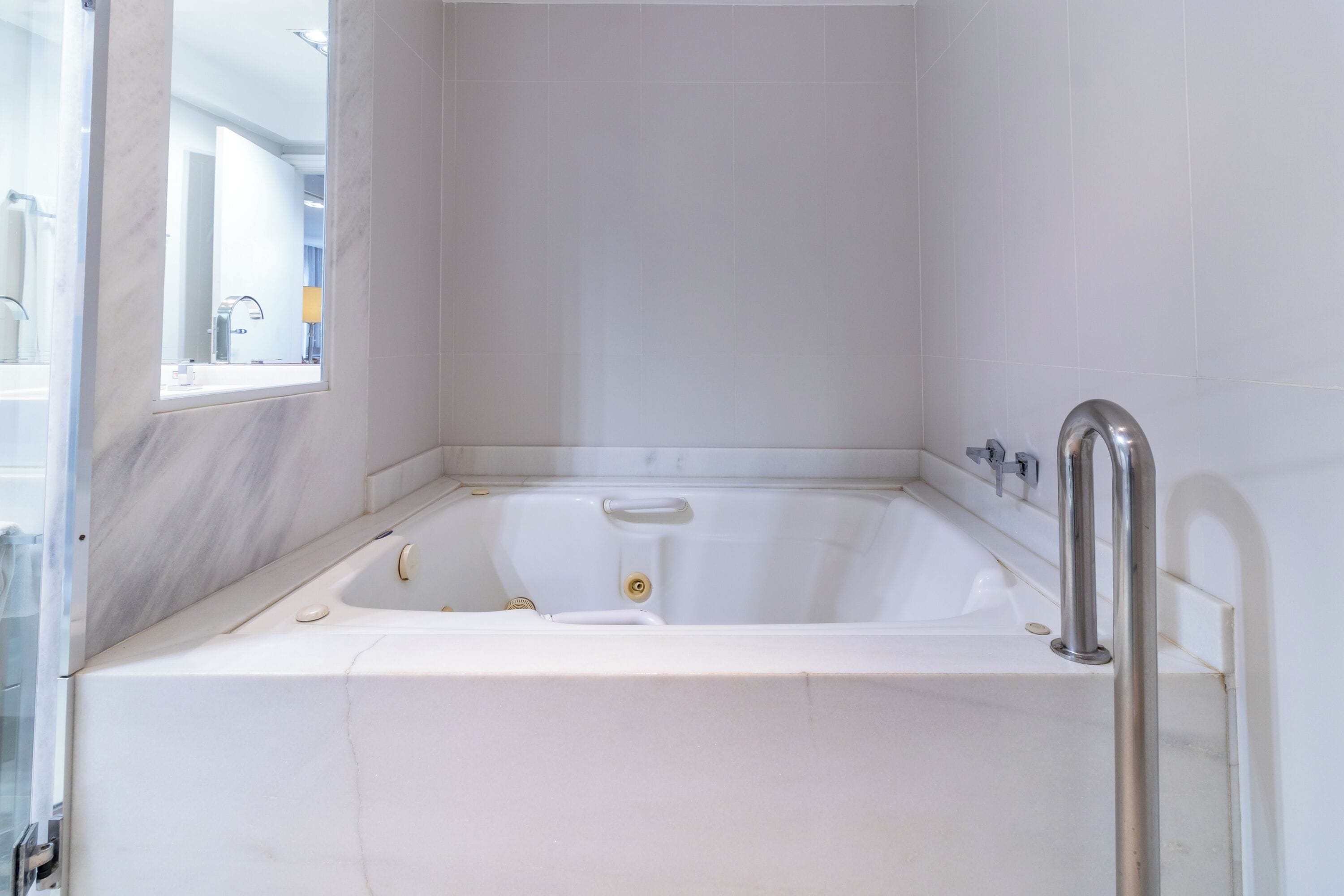 Une baignoire blanche équipée d’un pommeau de douche à main, avec une fenêtre et une porte en verre.