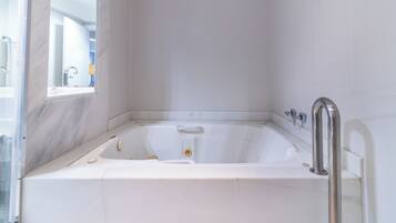 Une baignoire blanche équipée d’un pommeau de douche à main, avec une fenêtre et une porte en verre.