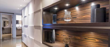 Un interior moderno con un muro decorado con madera, un florero de vidrio y un objeto cilíndrico negro en una estantería.