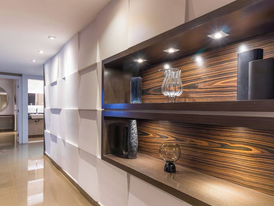Un interior moderno con un muro decorado con madera, un florero de vidrio y un objeto cilíndrico negro en una estantería.
